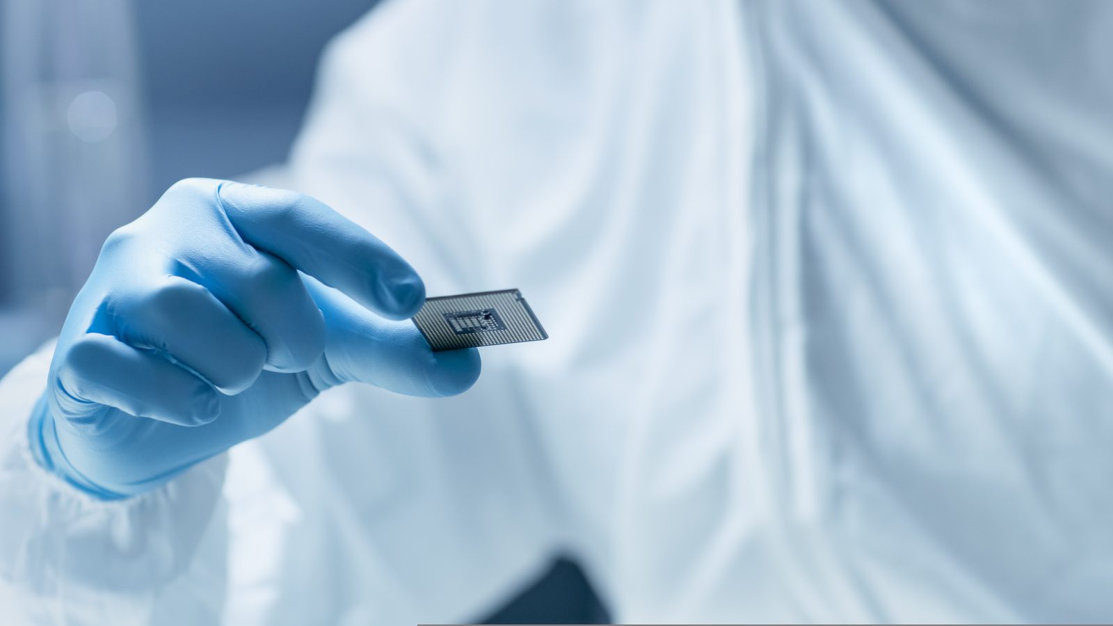 A gloved hand holding a microchip in a cleanroom