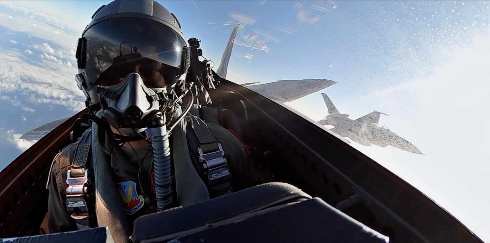 A pilot in a fighter cockpit with a wingman aircraft alongside